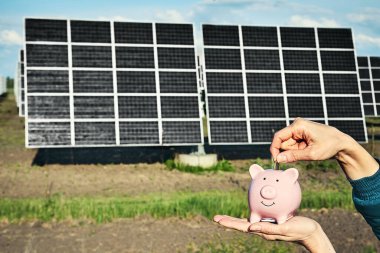 Arka planda fotovoltaik güneş enerjisi panelleri olan el ele tutuşma para banknotu, 