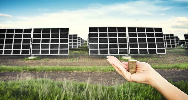 Hand holding money banknote with photovoltaic solar energy panels in background,