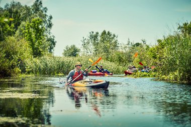 Bir grup genç kanoyla nehirde rafting yapıyor.