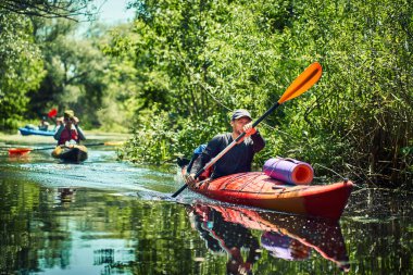 Bir grup genç kanoyla nehirde rafting yapıyor.