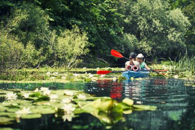 Bir grup genç kanoyla nehirde rafting yapıyor.