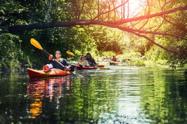 Bir grup genç kanoyla nehirde rafting yapıyor.