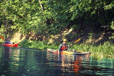 Bir grup genç kanoyla nehirde rafting yapıyor.