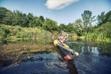 Bir grup genç kanoyla nehirde rafting yapıyor.