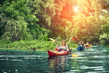 Bir grup genç kanoyla nehirde rafting yapıyor.