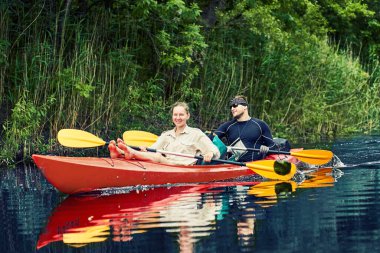Bir grup genç kanoyla nehirde rafting yapıyor.