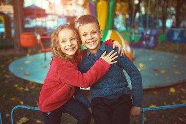 Güneşli bir sonbahar gününde parkta birlikte yürüyen parlak kazaklı iki küçük sevimli çocuk. Kardeşler arasındaki dostluk. Mutlu aile kavramı