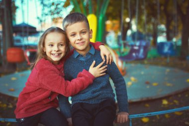 Güneşli bir sonbahar gününde parkta birlikte yürüyen parlak kazaklı iki küçük sevimli çocuk. Kardeşler arasındaki dostluk. Mutlu aile kavramı