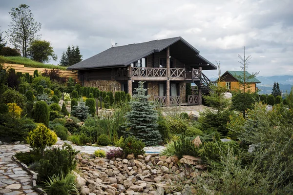 Köylü ahşap kulübesi, yemyeşil bahçe ve taş patikayla çevrili..