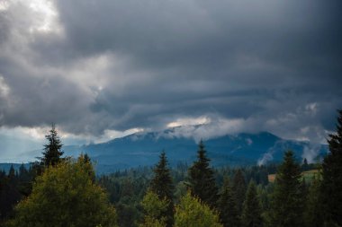 Ormanlı bir dağ manzarası üzerinde dramatik bulutlu gökyüzü.