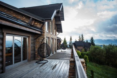 Geniş güverteli, sallanan sandalyeli, dağ manzaralı modern ahşap kulübe..