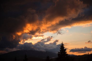 Dağ manzarası üzerinde kara bulutlarla dramatik bir gün batımı.