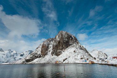 Mavi gökyüzünün altında sakin bir fiyort ile karla kaplı bir dağ. Lofoten Adaları, Norveç