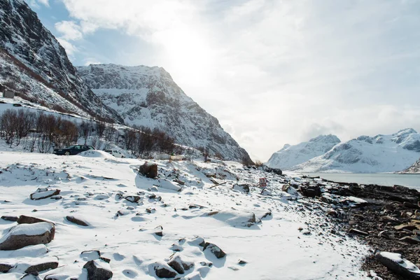 Parlak bir gökyüzünün altında kayalık kıyı şeridi olan karla kaplı dağ manzarası.