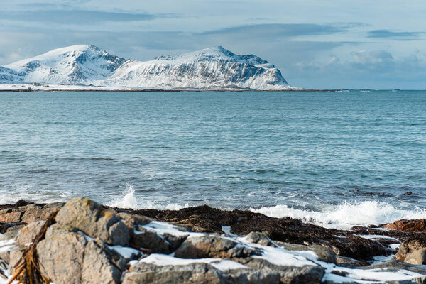 Snow-covered mountains by a rocky seashore with waves. Lofoten islands, Norway