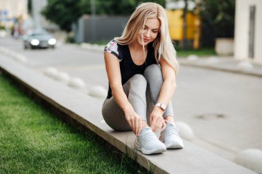 Dışarıda bir kaldırımda otururken bağcıklarını bağlayan sevimli sarışın kadın..