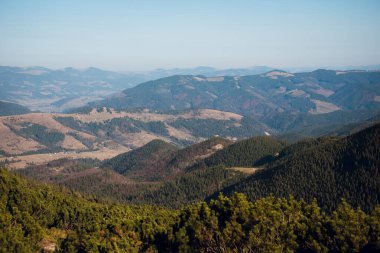 Mavi gökyüzünün altında yuvarlanan tepelerin ve dağların manzarası..