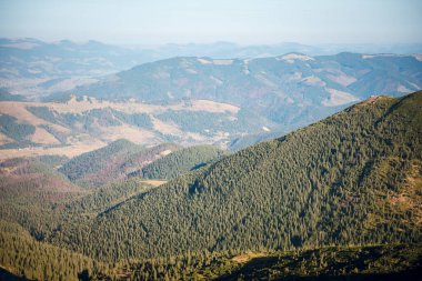 Berrak mavi gökyüzünün altındaki yemyeşil dağlar ve vadilerin havadan görünüşü.