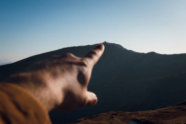 Açık mavi gökyüzünün altındaki uzak bir dağın tepesini gösteren bir el..