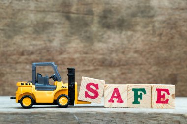 Sarı oyuncak forklift tutun ahşap arka plan üzerinde güvenli kelime tamamlamak için mektup blok S