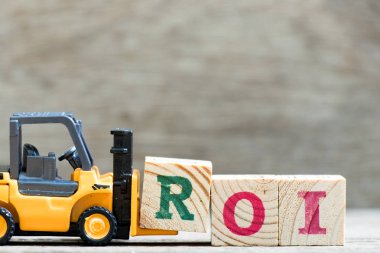 Oyuncak forklift tutun mektup blok içinde kelime ROI (yatırım dönüş kısaltması) ahşap arka plan üzerinde