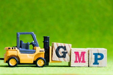 Oyuncak forlift tutun yeşil arka plan üzerinde kelime Gmp (kısaltma, iyi Manufacturinc Practice) yerine getirmek için mektup blok G