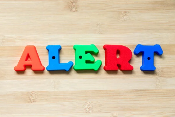 Color plastic alphabet in word alert on wood background