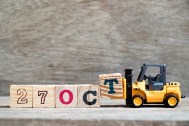 Ahşap arka plan (takvim tarihi Ekim ayında konsepti üzerinde 27 Ekim kelime tamamlamak için oyuncak forklift tutun blok T)