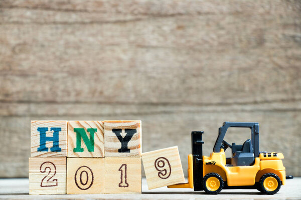 Игрушечная желтая фортепиано держит букву 9 для завершения слова HNY 2019 (аббревиатура Happy new year) на деревянном фоне
