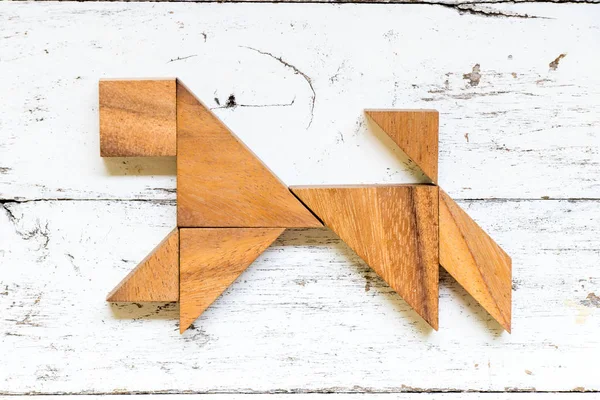 Tangram puzzle in running dog shape on old white wood background