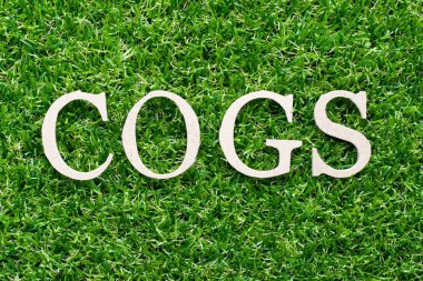 Kelime çarkları (kısaltma, satılan malların maliyetini) alfabesinde suni yeşil çim zemin üzerine ahşap