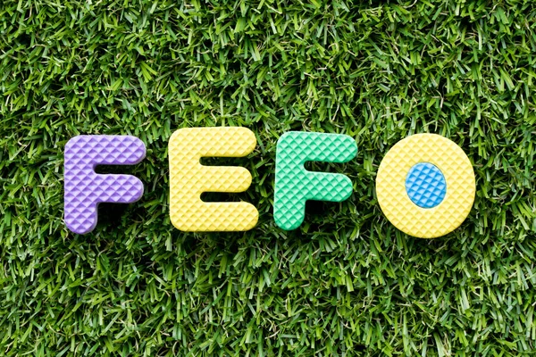 Color alphabet letter in word FEFO (abbreviation of first expired first out) on artificial green grass background