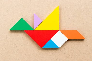Kuş şekli ahşap arka plan üzerinde uçan renk tangram bulmacanın
