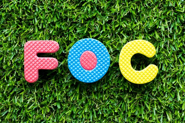 Color alphabet letter in word FOC (Abbreviation of Free of charge) on artificial green grass background