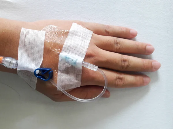 Patient hand with the tube of normal saline infusion on white cloth background