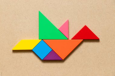 Kuş şekli ahşap arka plan üzerinde uçan renk tangram bulmacanın