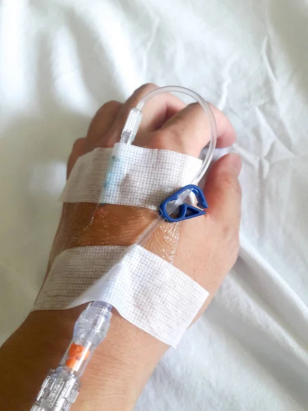 Patient hand with the tube of normal saline infusion on white cloth background