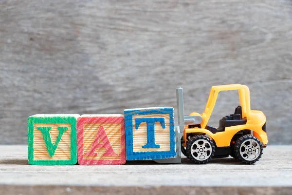 Toy forklift hold color letter block T to complete word VAT (Abberviation of Value added tax) on wood background