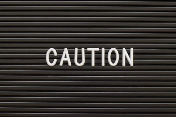 Black color felt letter board with white alphabet in word caution background