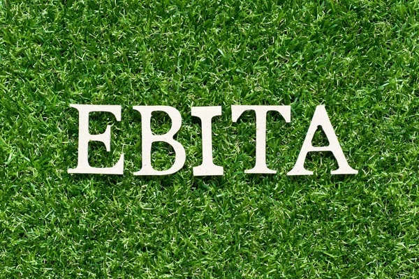 Alfabeto de madera letra en palabra EBITA (abreviatura de ganancias antes de intereses, impuestos y amortización) sobre fondo de hierba verde artificial —  Fotos de Stock
