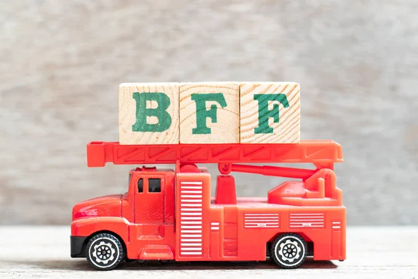 Red fire truck hold letter block in word BFF (Abbreviation of best friend forever) on wood background