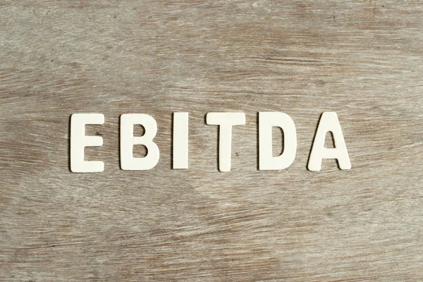 stock image Alphabet letter in word EBITDA (abbreviation of earnings before interest, taxes, depreciation and amortization) on wood background