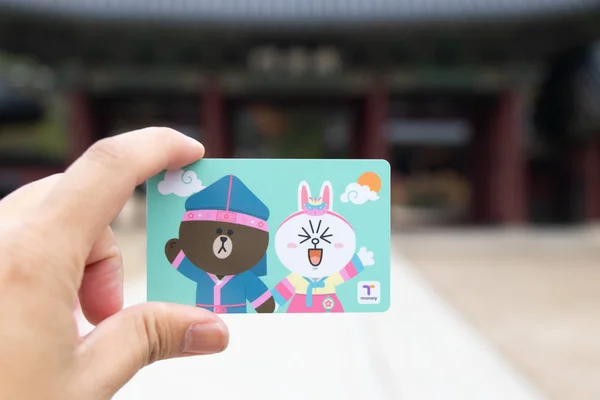 Seoul, South Korea- Sep 7, 2018  : Traveller hand hold t money card with line cartoon character on defocused Korean palace background. T Money is a prepaid card for travelling with train, bus and shopping in South Korea