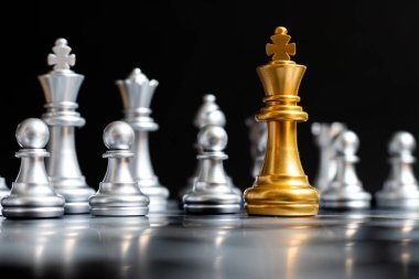 Altın Kral satranç parçası siyah arka planda başka bir gümüş takım yüz (liderlik kavramı, sorun veya kriz durumu)