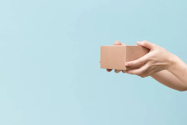 La mano de la mujer sostiene la caja acanalada marrón sobre fondo de pared azul — Foto de Stock