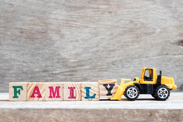 Spielzeug Bulldozer halten Buchstabenblock y, um Wortfamilie auf Holz-Hintergrund zu vervollständigen — Stockfoto