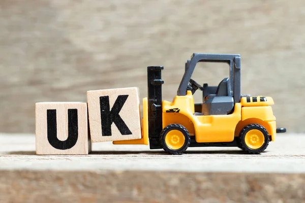 Toy vorkheftruck hold letter block k to complete word UK (afkorting van verenigd koninkrijk) on wood background — Stockfoto