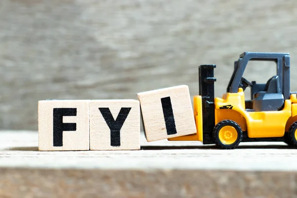 Empilhadeira de brinquedo segurar letra bloco I para completar a palavra FYI (Abreviatura de Para sua informação) sobre fundo de madeira — Fotografia de Stock