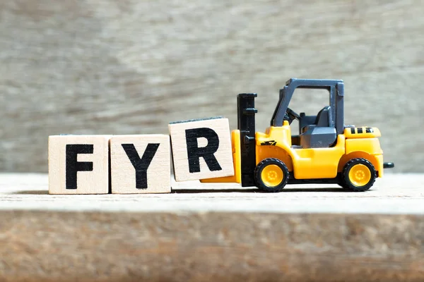 Toy forklift hold letter block R to complete word FYR (abbreviation of for your reference) on wood background