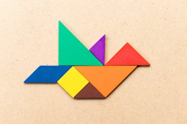 Kuş şekli ahşap arka plan üzerinde uçan renk tangram bulmacanın